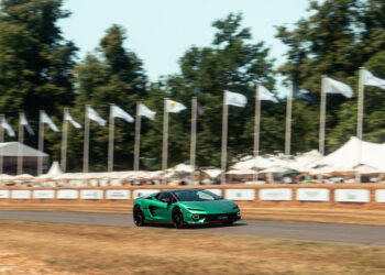 A green Lamborghini Temerario speeds along the track at Goodwood, with white flags and tents in the background, surrounded by trees.