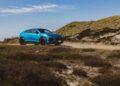 A Lamborghini Urus SE is parked on a dirt road surrounded by grassy dunes and shrubs under a clear blue sky, capturing the spirit of Sylt during an exclusive event.