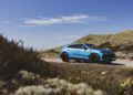 A blue Lamborghini Urus SE is parked on a dirt road surrounded by grassy hills under a clear blue sky, ready for an exclusive event on Sylt.