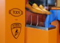 A pair of tan loafers displayed in a clear case beside an orange panel with Tod's and Lamborghini logos, showcased at an Exclusive Event.
