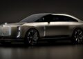 A sleek, silver Bentley EV SUV concept car with an illuminated grille and accents, black roof, and large black wheels, shown in a dimly lit studio setting.