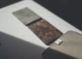 Three rectangular samples, including a brown textured tile and a gray one, are laid out on a white surface beside a beige fabric pouch, showcasing Bentley Mulliner interior options.