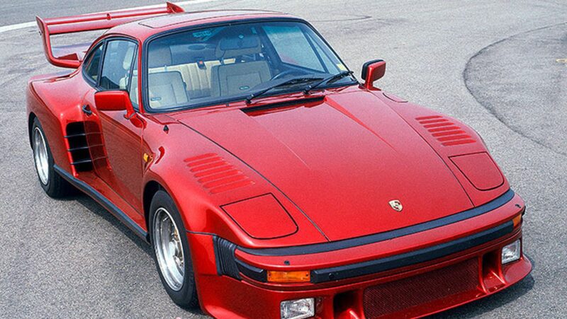 A red classic Porsche sports car with a large rear wing, likely inspired by exclusive customer requests, is parked on a paved surface.