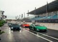 Five brightly colored sports cars, including the Lamborghini Temerario and V12 Revuelto, are parked in a row on a wet racetrack beside empty grandstands under an overcast sky, ready for a track review.