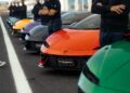 Several Lamborghini sports cars, including the V12 Revuelto, are lined up on the track as people stand beside each car with arms crossed, ready for a thrilling track review.