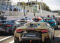 Several Lamborghini supercars, including the V12 Revuelto, are parked in a row on a racetrack with people and seating visible in the background—an impressive scene perfect for a Track Review.