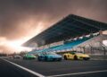 A row of brightly colored sports cars, including the Lamborghini Temerario and V12 Revuelto, is lined up on a racetrack in front of empty grandstands at sunset under a cloudy sky—perfect for a thrilling track review.