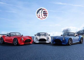 Three sports cars—red, white, and blue—are parked on asphalt under a blue sky with a logo featuring the letters "AC" and an American flag design above them.