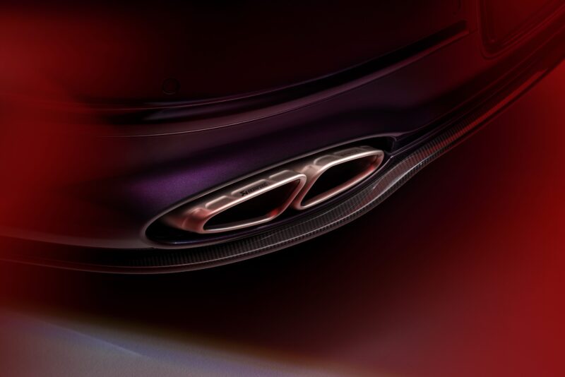 Close-up view of the rear dual exhaust pipes of a car, with red lighting partially obscuring the image—highlighting the powerful exhaust note, crafted through a Bentley Motors and Akrapovič partnership.