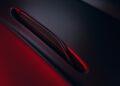 Close-up of a 2026 Aston Martin Vanquish S hood vent with a red light reflecting off the dark, smooth surface.