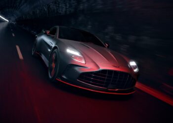 A matte gray 2026 Aston Martin Vanquish S with headlights on speeds through a dimly lit tunnel, its blurred surroundings emphasizing its dynamic presence.