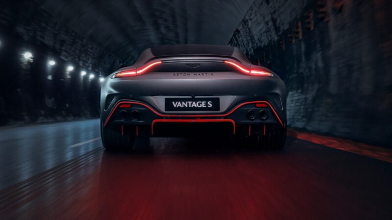 A rear view of a grey 2026 Aston Martin Vanquish S driving through a dimly lit tunnel with its taillights illuminated.