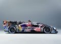 A BMW Le Mans race car with a colorful, abstract livery is photographed in profile against a plain, light gray background, capturing the spirit of Monterey Car Week 2025.