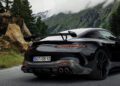 A black AMG GT with a rear spoiler is parked on a mountain road, surrounded by trees, rocks, and misty mountains in the background.