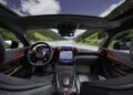 Interior view of a luxury AMG GT with black and red accents, digital dashboard, and a large central touchscreen, overlooking a mountain road and landscape through the windshield.