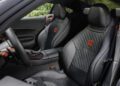 The image shows the interior of a modern sports car, reminiscent of an AMG GT, with black and red accents, quilted leather seats, and detailed stitching on the seats and dashboard.
