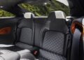 Rear seats of this hybrid supercar feature black and grey patterned leather upholstery, red seatbelt slots, and a view of green hills through the rear window.