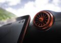 A close-up of a BRABUS-tuned car’s red circular air vent next to a tablet-like touchscreen display showing part of a map, with an out-of-focus landscape visible through the window.