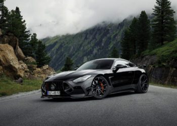 A BRABUS AMG GT hybrid supercar is parked on a mountain road, surrounded by trees and rocky cliffs with misty mountains in the background.