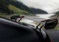 Close-up of a carbon fiber rear wing spoiler on a black AMG GT Hybrid Supercar, parked near a lake surrounded by mountains and greenery.