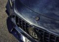 Close-up of a blue carbon fiber BRABUS Rocket GTS car hood and grille in Deep Blue, showcasing the Brabus badge and a “BOT B 8” license plate on a paved surface.