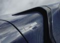Close-up of a car with a Deep Blue carbon fiber finish, showing a "Rocket GTS" badge and part of the vehicle's aerodynamic design against a cloudy sky background.