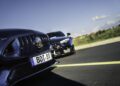 Close-up of two luxury cars parked on an asphalt road under a clear sky, with the focus on the blue car’s front grille and a license plate reading "BOT B 8".