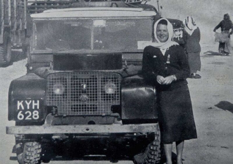 A woman in a headscarf stands beside a vintage vehicle with license plate KYH 628, evoking the spirit of Land Rover Classic’s upcoming showcase of 10 Historic Expedition Icons at the 2025 Pebble Beach Concours d'Elegance.