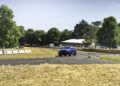 A blue Bentley Bentayga Speed SUV drives on the Goodwood Hillclimb racetrack, surrounded by hay bales, with trees and a white tent structure in the background, aiming for a record performance.