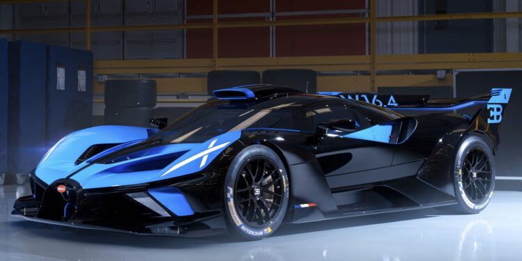 A sleek black and blue Bugatti Bolide hypercar is parked indoors under bright lights, showcasing its aerodynamic design and racing features.