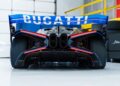 Rear view of #001 of 40 Track-Only Bugatti Bolide set for auction debut at Pebble Beach in a garage, showcasing its large rear wing, central exhaust pipes, and aerodynamic design features.