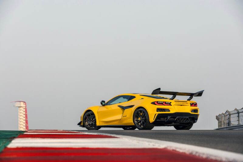 A yellow Corvette ZR1 with a large rear wing is parked on a racetrack near a red, white, and green curb under a clear sky, ready for a Track Review that proves 1000 HP doesn’t need a seven-figure price.