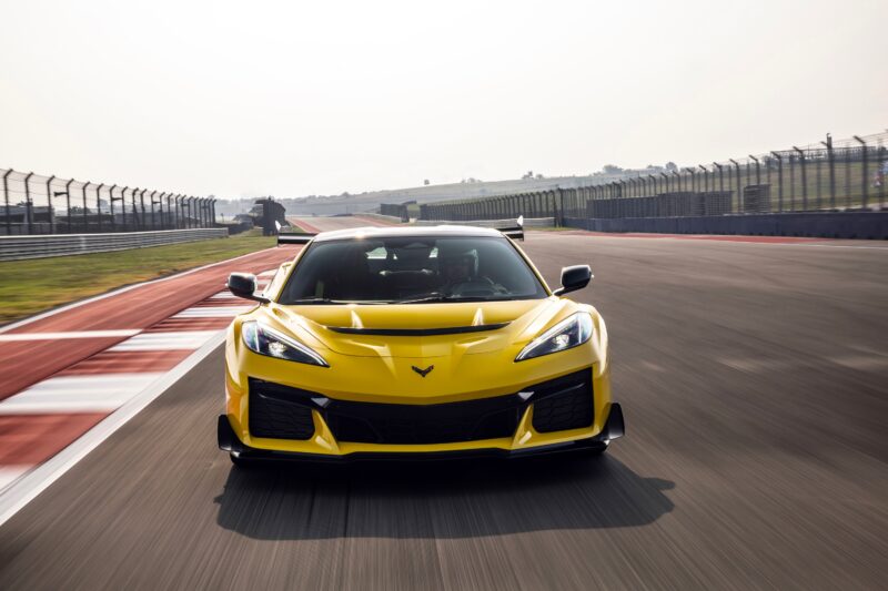 A yellow sports car drives on a racetrack, viewed from the front with blurred pavement and fencing in the background—a true Track Review Corvette ZR1 proves 1000 HP doesn’t need a seven-figure price.