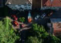 Aerial view of a courtyard with several red Ferrari sports cars, a brown boat, and other vehicles parked near two large buildings surrounded by greenery—perfect for a Cavallino Classic Concours Event setting.