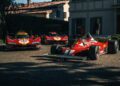 Three red Ferrari race cars, including a classic Formula 1 car and two modern prototypes, are parked on a cobblestone driveway in front of a house during a prestigious Cavallino Classic Ferrari event.