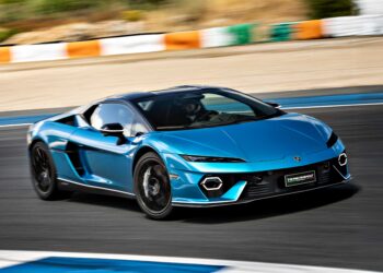 A blue V12 Revuelto Lamborghini is driving on a racetrack with a blurred background, indicating motion.