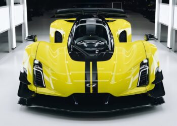 A bright yellow, high-performance Czinger C21 with black stripes is displayed in a brightly lit, modern showroom as Prestige Imports delivers this bespoke masterpiece in Miami.