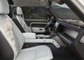 The interior of a modern Defender showcases recent design updates, with white leather seats, a touchscreen display, and mountain scenery visible through the windows.