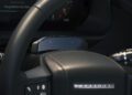 Close-up of a Defender's steering wheel and dashboard, highlighting control stalks, part of the instrument panel, and a small black device above the wheel—showcasing recent design updates.