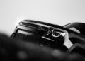 Close-up, angled view of the front end of a 2026 Land Rover Defender in OCTA Black, highlighting the grille, headlight, and part of the hood in striking black and white.
