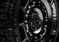 Close-up view of a Battle-Ready OCTA Black alloy wheel on the 2026 Land Rover Defender, with "DEFENDER" on the center cap, showing sharp tire tread and detailed spokes in low light.