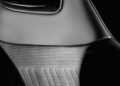 Close-up of an OCTA Black Land Rover Defender car seat with perforated and textured leather upholstery, showing part of the seatback and headrest in soft lighting. Model year 2026.