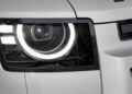 Close-up of a modern Defender's left headlight with LED ring and geometric design updates, set in a white body panel.