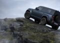 A blue Defender SUV drives up a steep, rocky incline under a cloudy sky, showcasing its off-road capability and latest design updates.