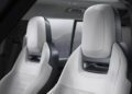 Two modern, light-colored car seats are shown inside a Defender, with design updates evident in the sleek lines. A window reveals a blurred outdoor mountain view in the background.