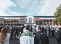 A large crowd gathers outside the Bentley design studio, facing a stage with large screens on a cloudy day.