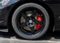 Close-up of a black car's front wheel with a five-spoke black rim, red brake caliper, and Michelin tire—parked on the street. Bid On This 2010 Dodge Viper SRT-10 Roadster ACR With Just 20 Miles for your chance to own it.