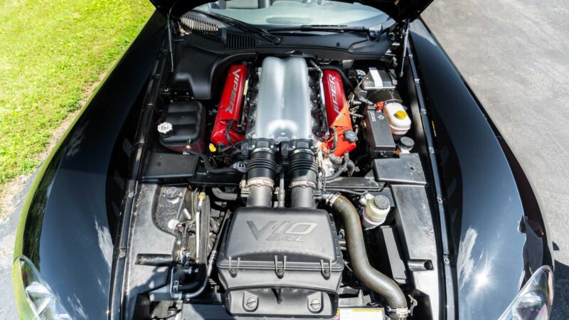 A V10 8.4L engine is shown under the hood of a car, with red engine covers and various components visible—Bid On This 2010 Dodge Viper SRT-10 Roadster ACR With Just 20 Miles for a chance to own this powerhouse.