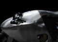 A close-up of a modern motorcycle with a sleek, metallic silver fairing and black seat, set against a black background—true rideable art that embodies the elegance of futuristic aluminum sculpture.