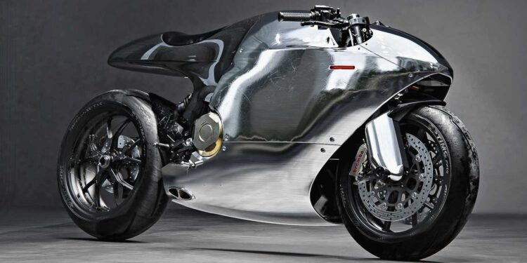A sleek, modern motorcycle with a reflective, polished metal body and minimalist design sits on a gray studio floor, resembling a piece of futuristic sculpture.